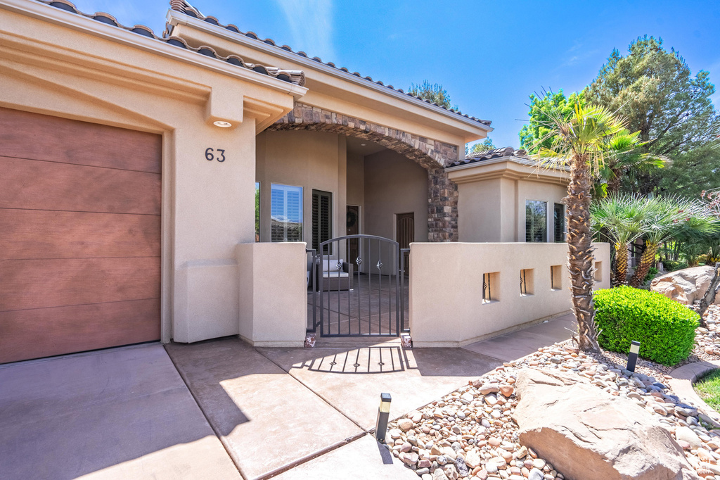 Property entrance with a gate, stone siding, a tiled roof, fence, and stucco siding
