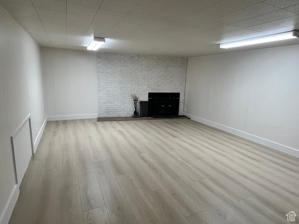 Finished below grade area with baseboards, a brick fireplace, and wood finished floors