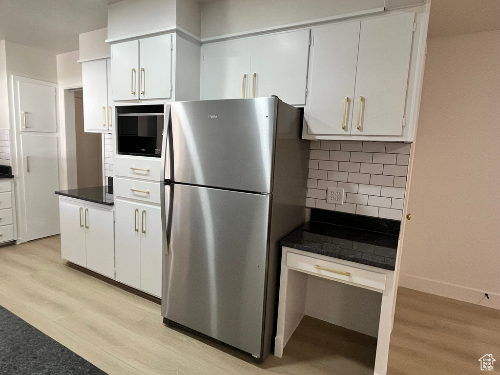 Kitchen with backsplash, white cabinetry, light wood-type flooring, and freestanding refrigerator
