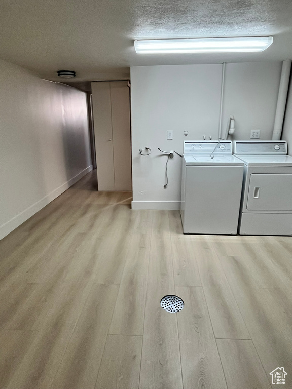 Laundry room featuring light wood finished floors, a textured ceiling, baseboards, washer and dryer, and laundry area