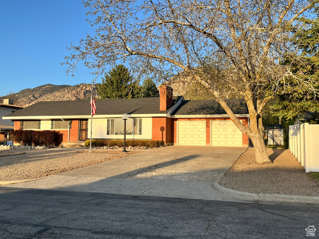 View of front of house with a mountain view, concrete driveway, fence, brick siding, and an attached garage