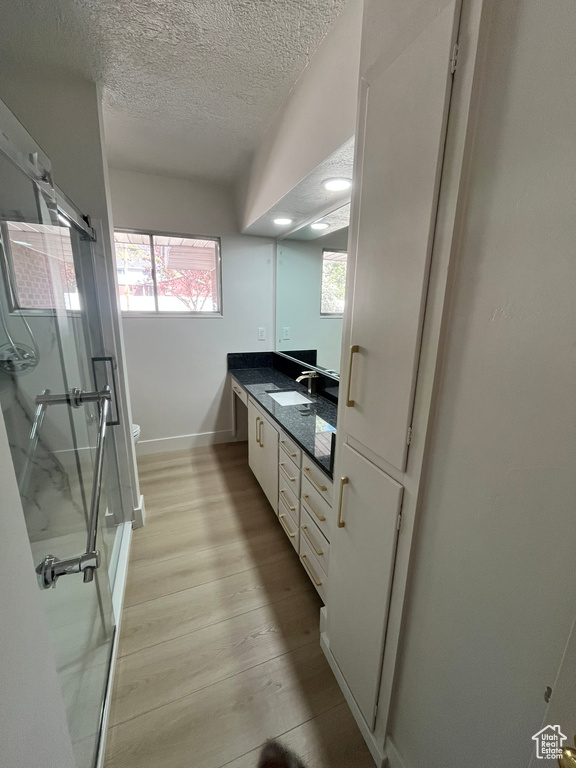 Bathroom with a textured ceiling, toilet, wood finished floors, a shower stall, and vanity