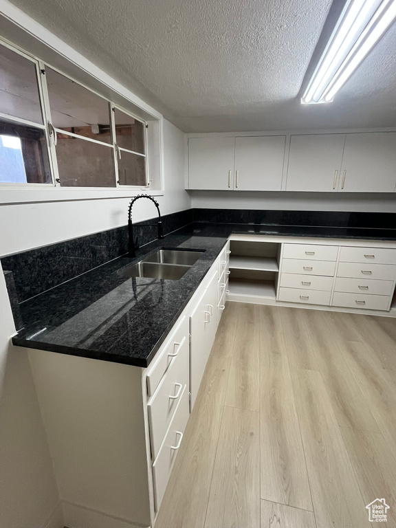 Kitchen with dark stone counters, a sink, a textured ceiling, light wood finished floors, and white cabinets