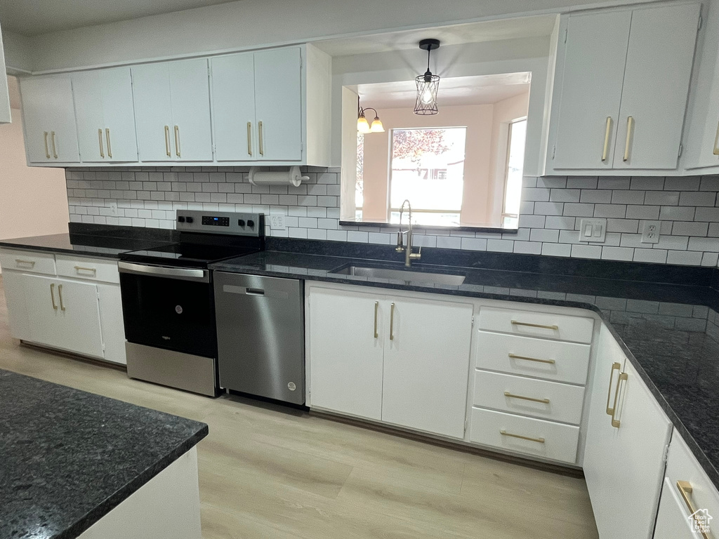 Kitchen featuring a sink, decorative backsplash, light wood-style floors, white cabinetry, and appliances with stainless steel finishes