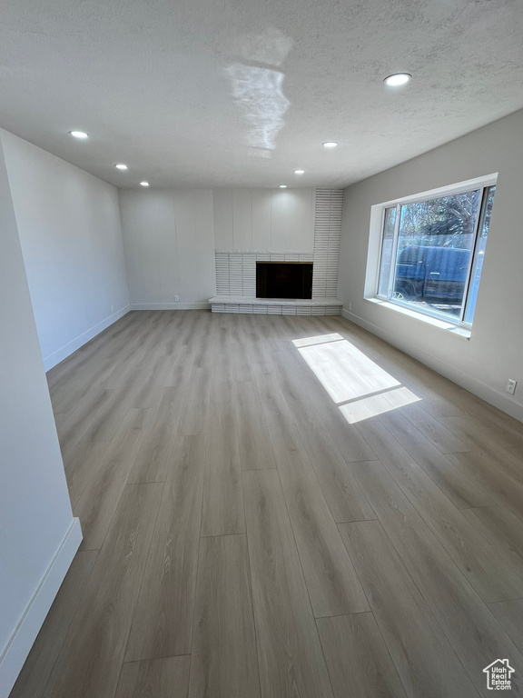 Unfurnished living room with light wood finished floors, a tiled fireplace, and baseboards