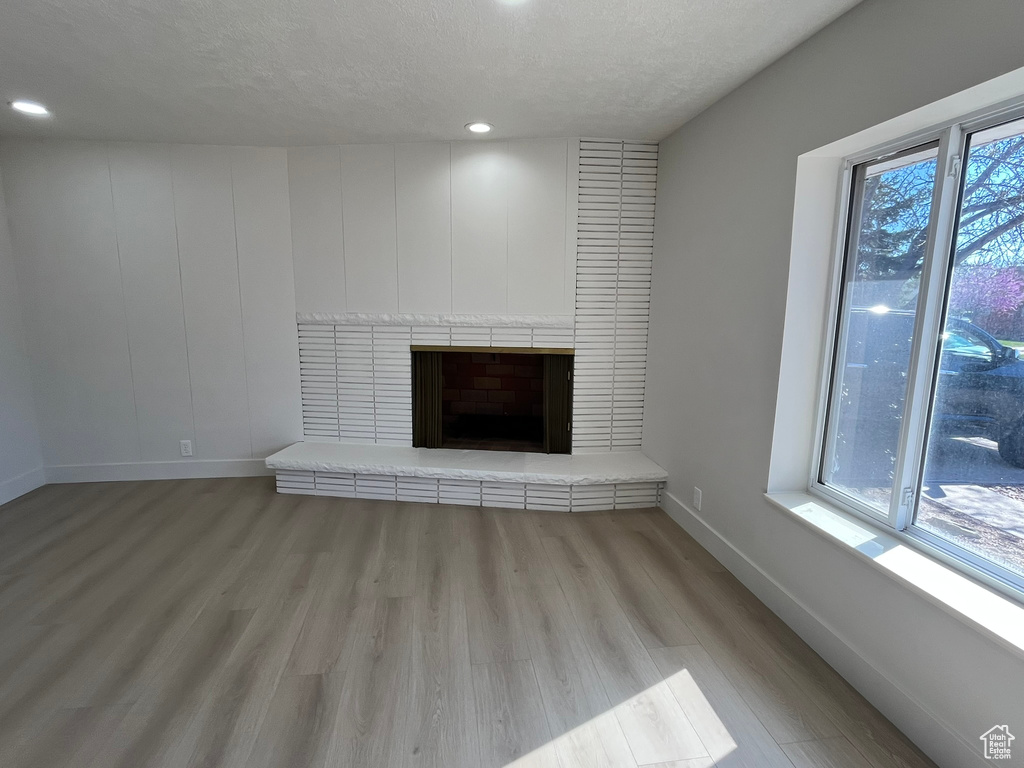 Unfurnished living room with a textured ceiling, light wood finished floors, baseboards, a brick fireplace, and recessed lighting