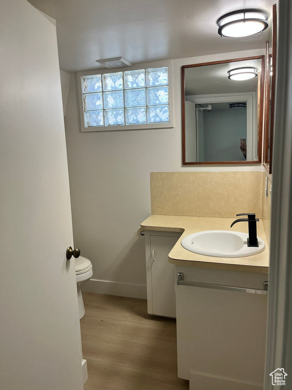 Half bathroom with baseboards, wood finished floors, toilet, and vanity
