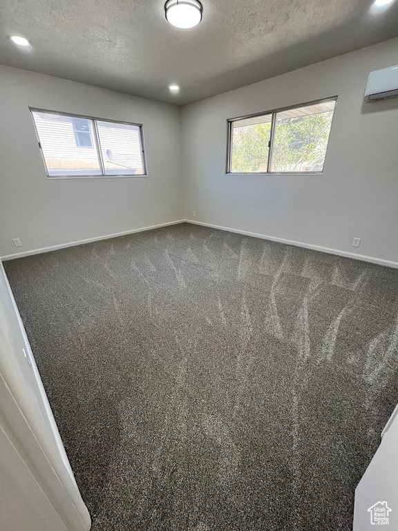 Spare room featuring carpet floors, baseboards, a textured ceiling, and a wall unit AC