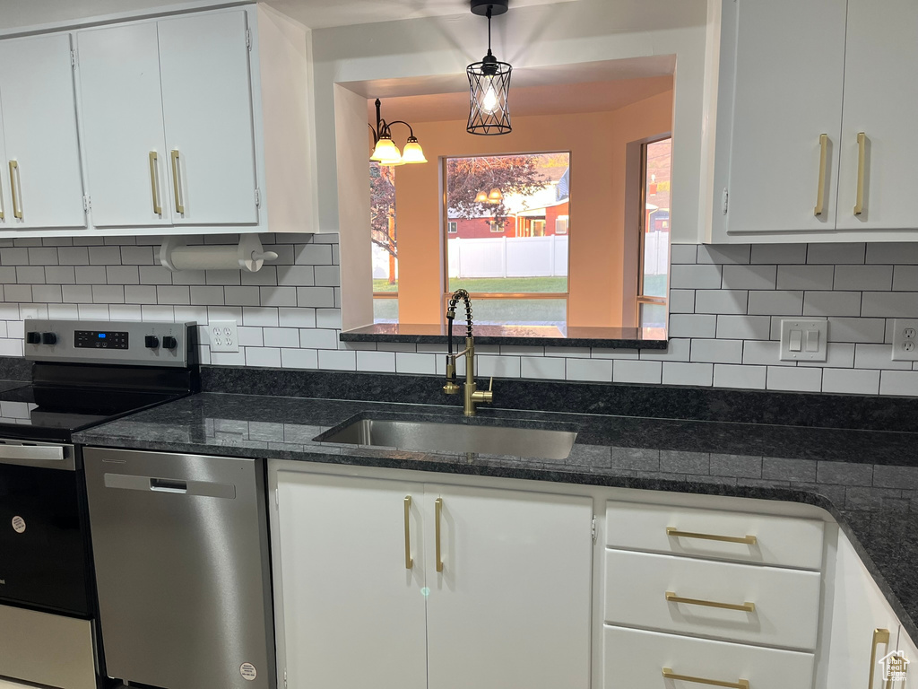 Kitchen with stainless steel appliances, a sink, dark stone counters, tasteful backsplash, and white cabinetry