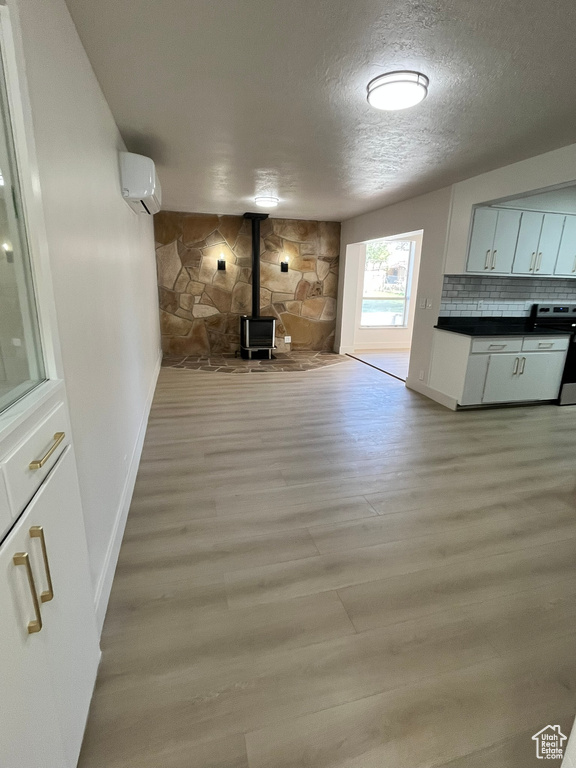 Unfurnished living room featuring baseboards, a wood stove, a textured ceiling, and light wood-type flooring