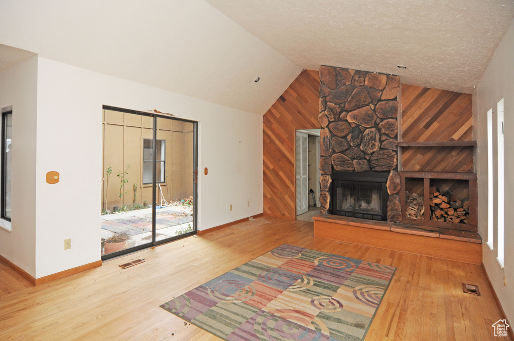 Unfurnished living room featuring lofted ceiling, baseboards, visible vents, a stone fireplace, and wood finished floors