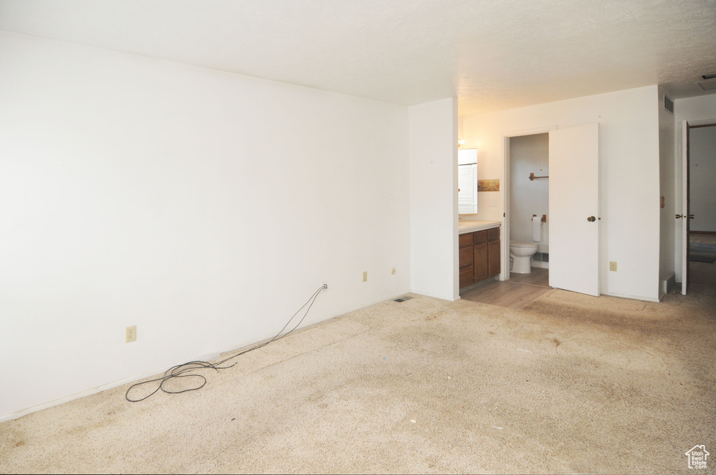 Unfurnished bedroom with connected bathroom and light carpet