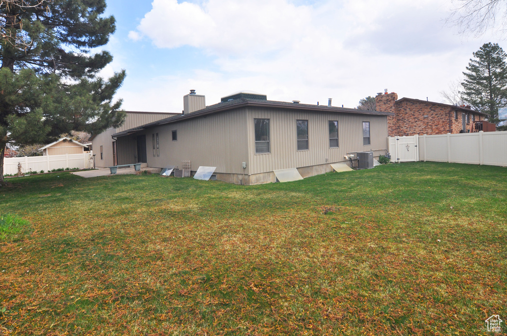 Rear view of house featuring a fenced backyard, a lawn, a chimney, and cooling unit