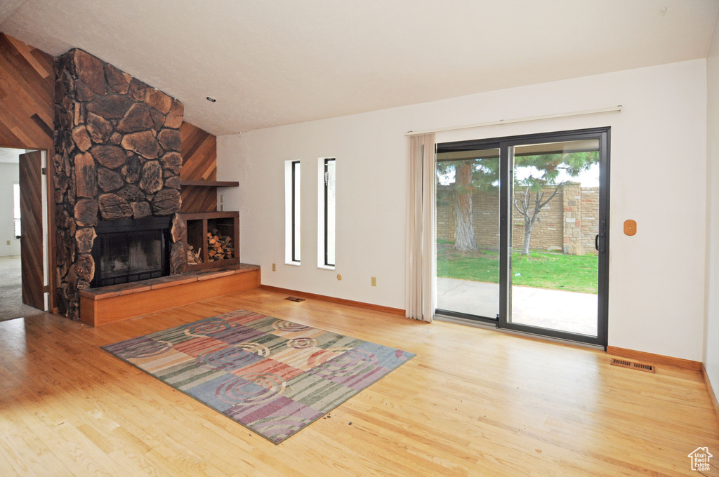 Unfurnished living room featuring visible vents, a stone fireplace, lofted ceiling, and wood finished floors