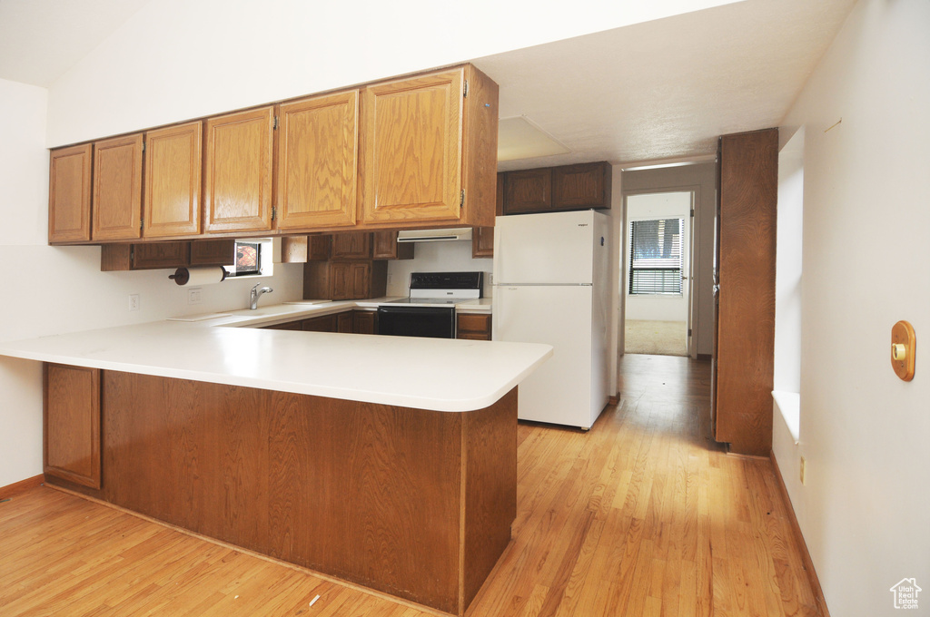 Kitchen with light countertops, a peninsula, electric stove, light wood-type flooring, and freestanding refrigerator