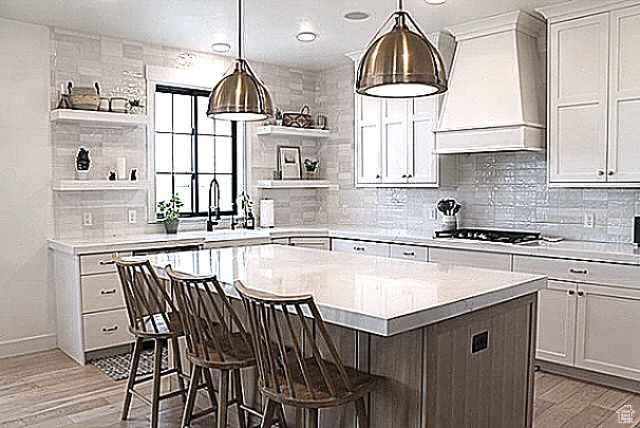 Kitchen featuring open shelves, cooktop, light countertops, and custom range hood