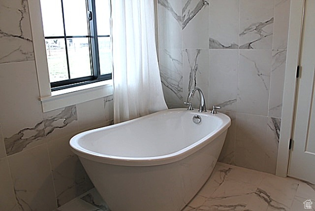 Full bathroom with tile walls, a soaking tub, and marble finish floor
