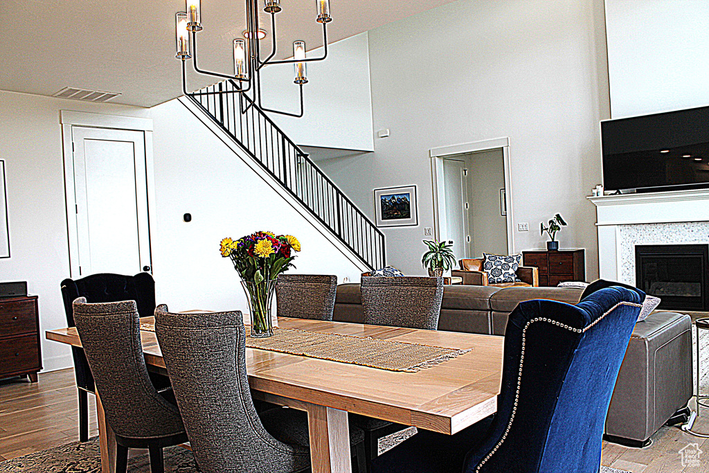 Dining space with wood finished floors, stairs, a high ceiling, a chandelier, and a glass covered fireplace