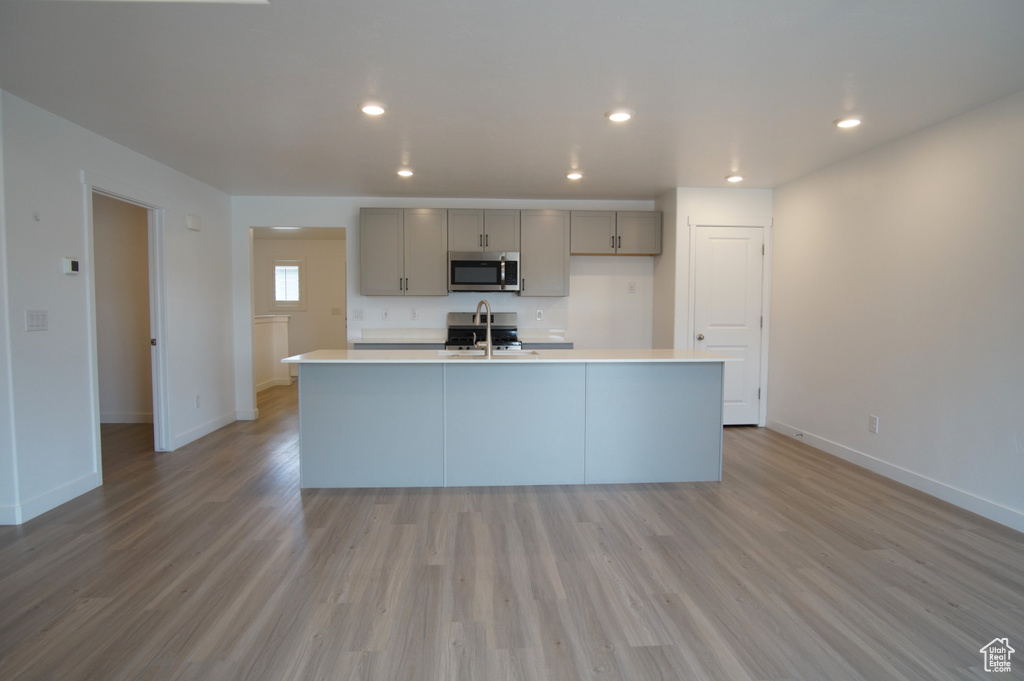 Kitchen featuring a sink, gray cabinets, light countertops, stainless steel microwave, and baseboards
