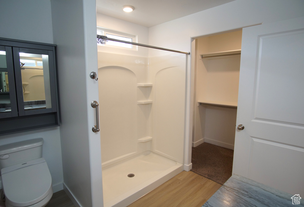 Full bath featuring baseboards, wood finished floors, toilet, and a stall shower