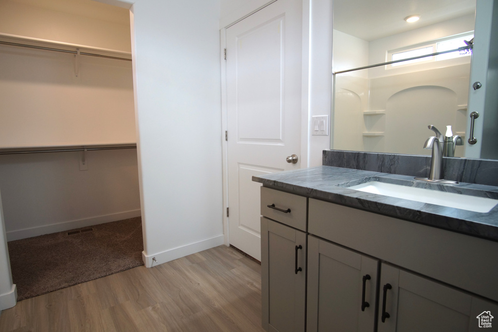 Full bathroom featuring baseboards, wood finished floors, a shower, vanity, and a walk in closet
