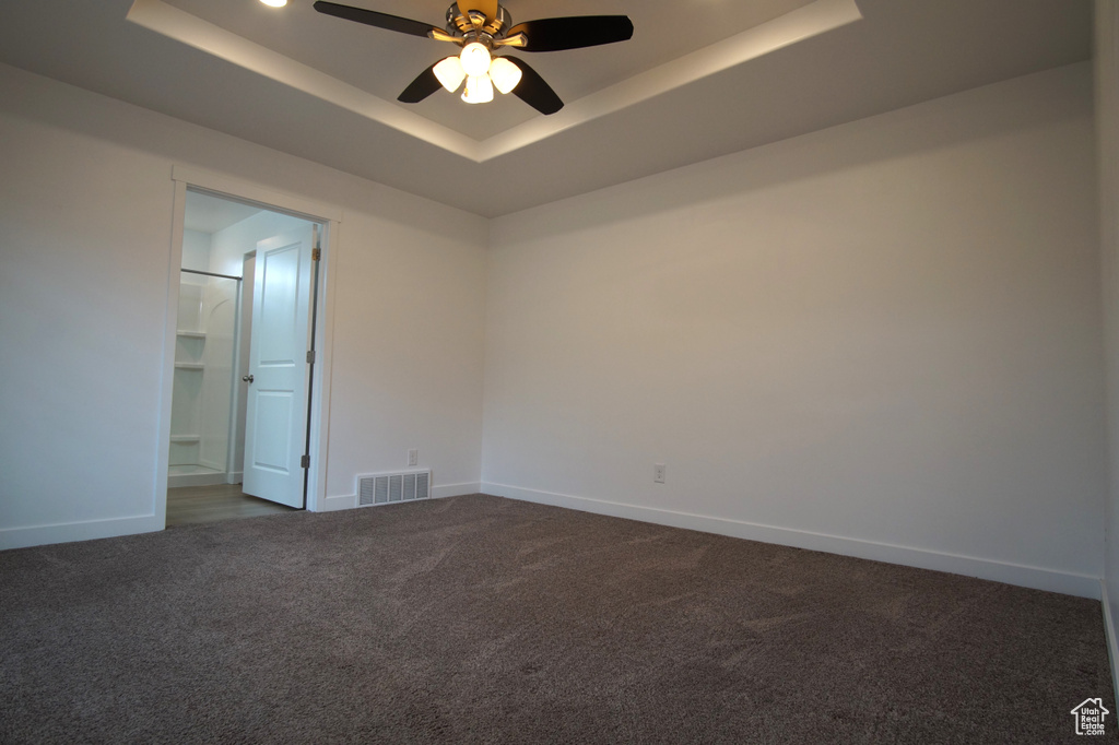 Unfurnished room with baseboards, visible vents, a ceiling fan, dark carpet, and a raised ceiling