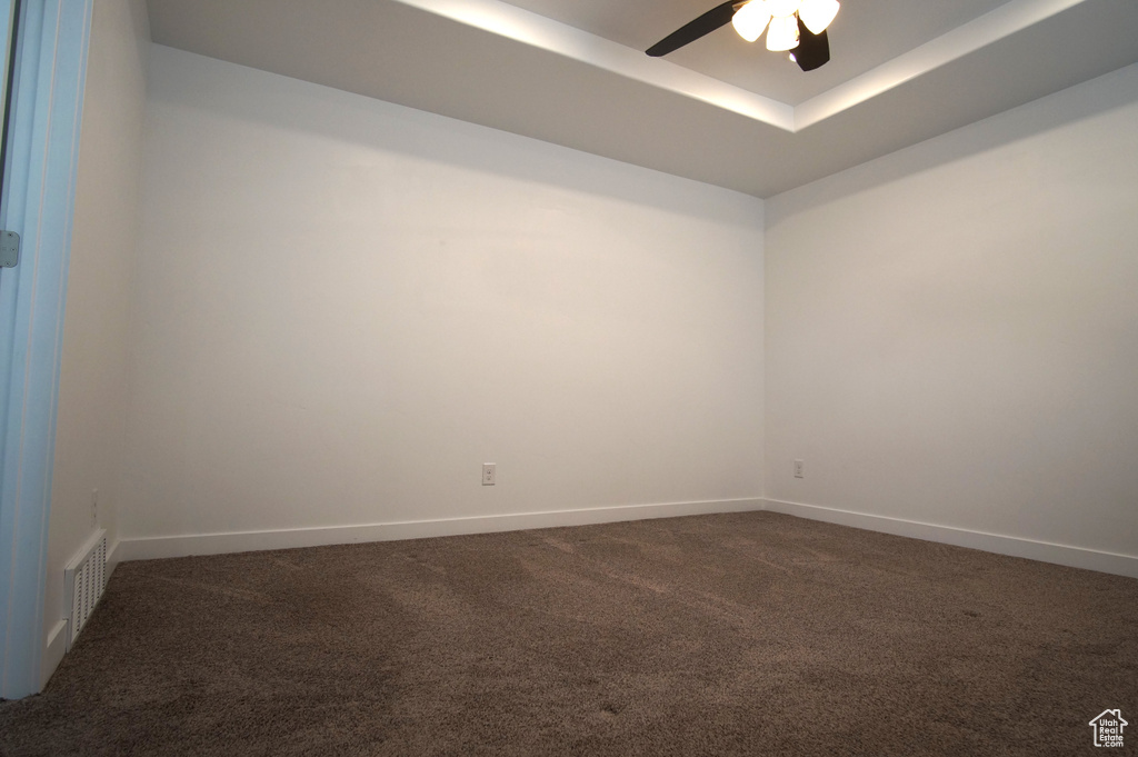 Carpeted spare room featuring baseboards, a ceiling fan, visible vents, and a raised ceiling