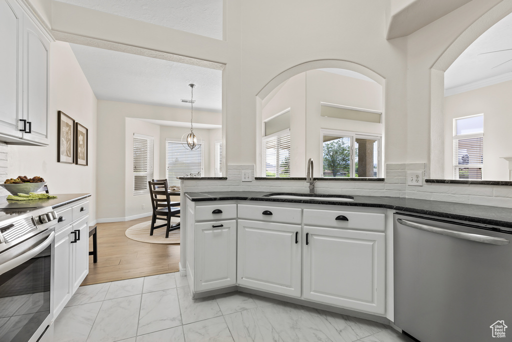 Kitchen with stainless steel appliances, a sink, light marble finish floors, white cabinets, and dark stone counters