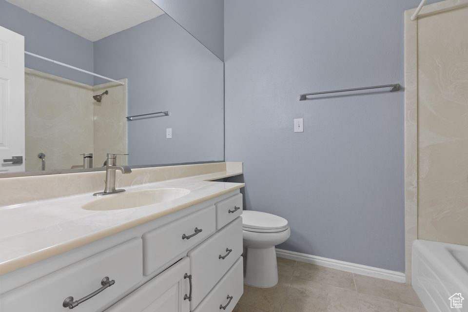 Bathroom with baseboards, toilet, vanity, tile patterned floors, and washtub / shower combination