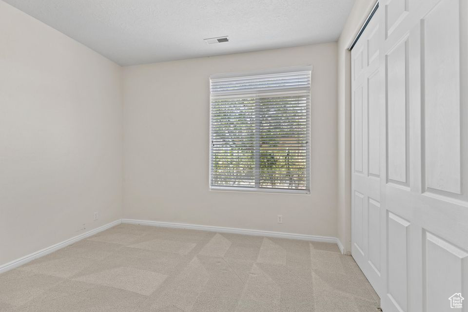 Unfurnished bedroom with baseboards, light carpet, a closet, and a textured ceiling