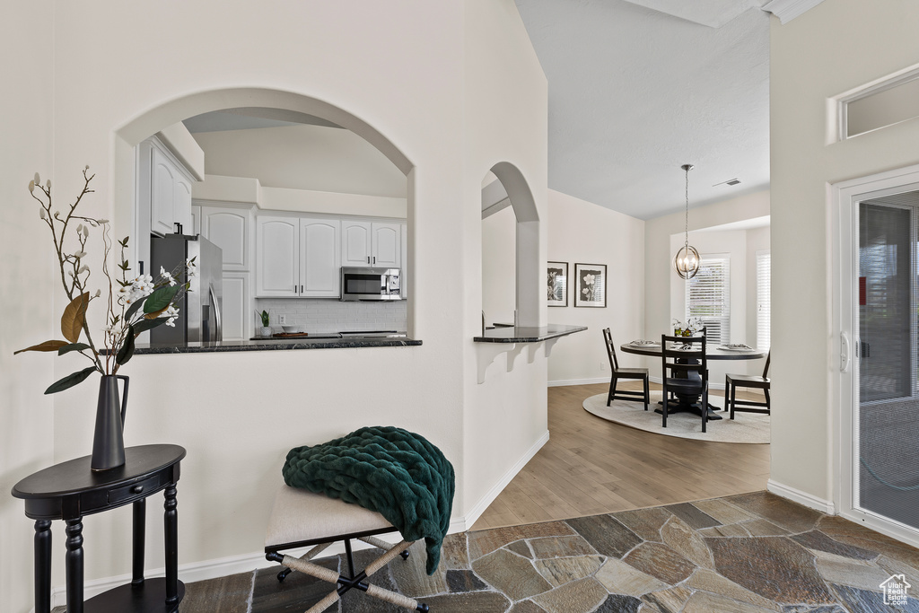 Kitchen with appliances with stainless steel finishes, dark countertops, a breakfast bar, white cabinets, and decorative light fixtures