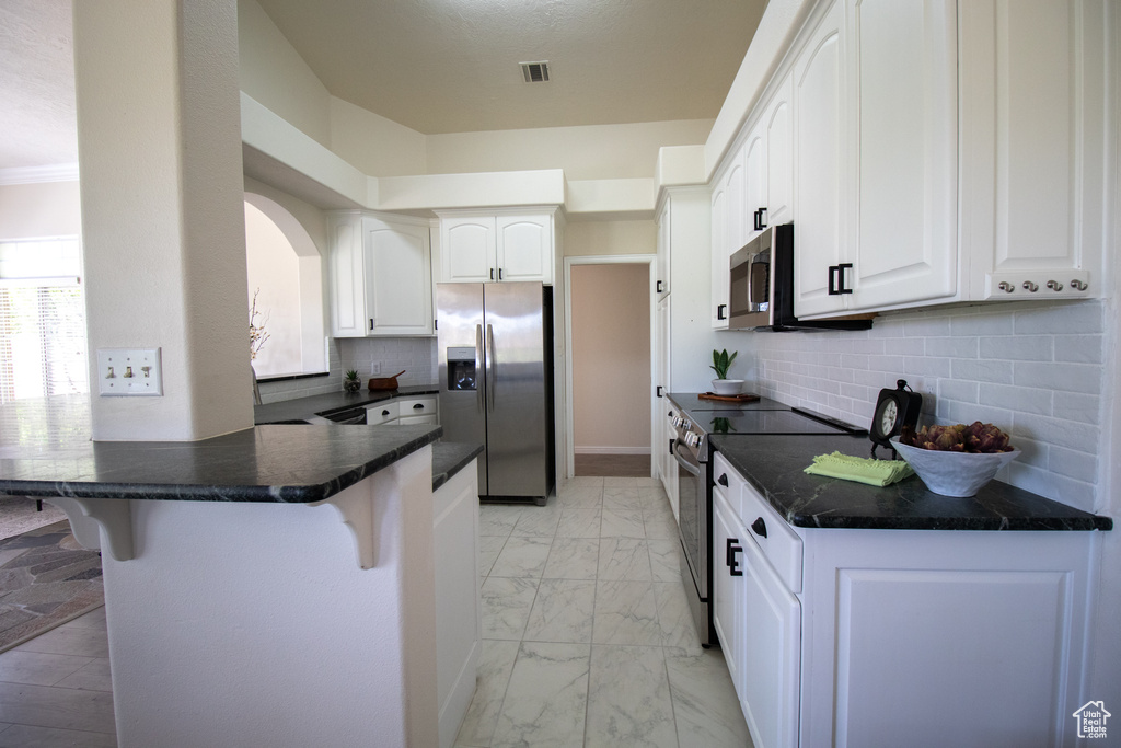 Kitchen with stainless steel appliances, a breakfast bar area, light marble finish floors, a peninsula, and white cabinets