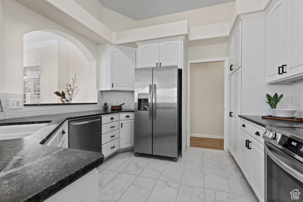 Kitchen featuring stainless steel appliances, light marble finish flooring, white cabinets, backsplash, and a sink