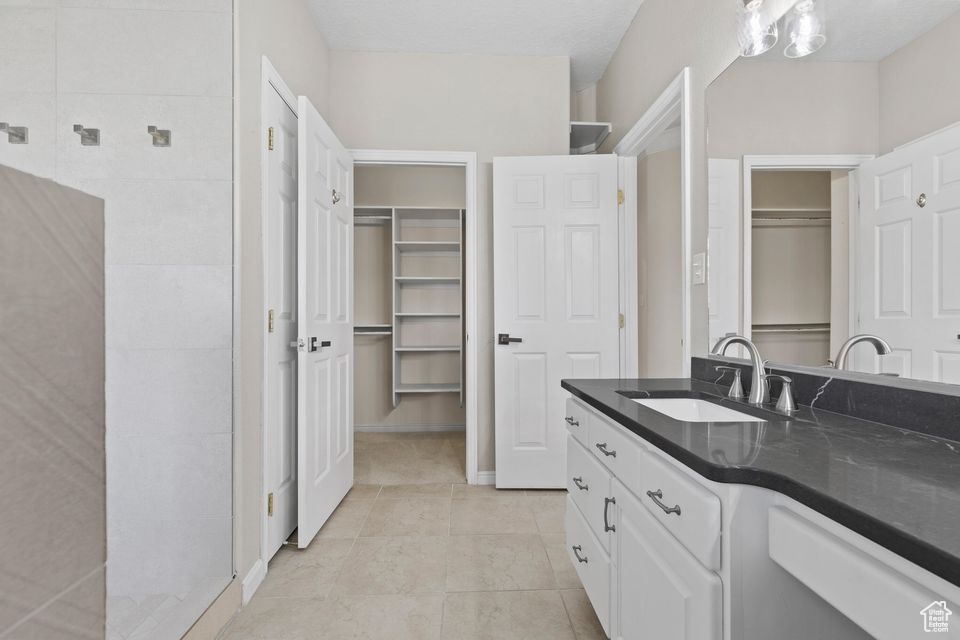 Full bath with vanity, a spacious closet, tile patterned flooring, and a shower