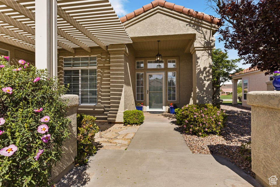 Property entrance with stucco siding, a tiled roof, and a pergola