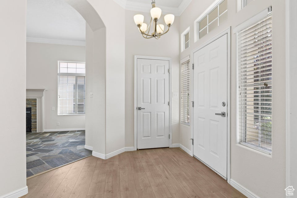 Foyer entrance featuring arched walkways, crown molding, a chandelier, light wood-style flooring, and baseboards