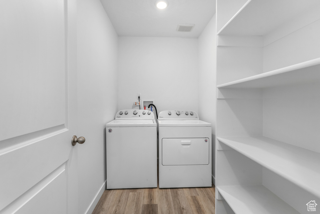 Clothes washing area with light wood finished floors, washer and dryer, and laundry area