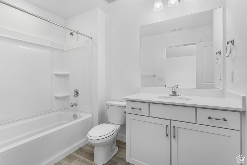Bathroom featuring wood finished floors, vanity,  shower combination, toilet, and visible vents