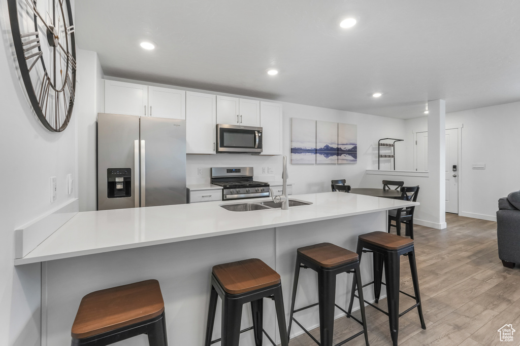 Kitchen with a breakfast bar area, stainless steel appliances, light wood finished floors, and a sink