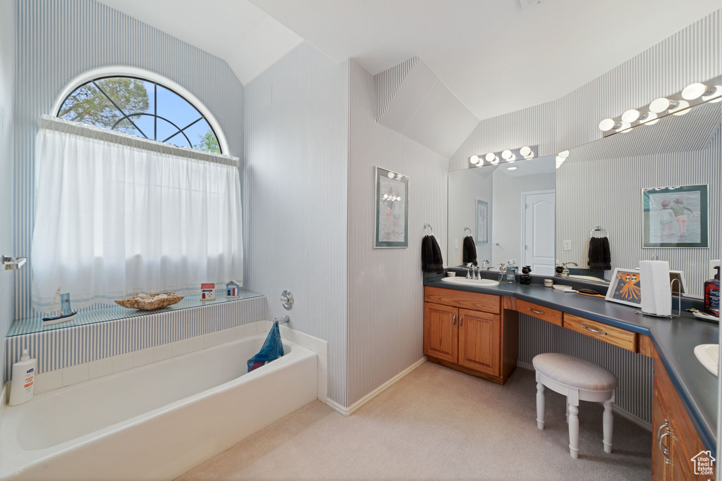 Full bath featuring a garden tub, lofted ceiling, a sink, and double vanity