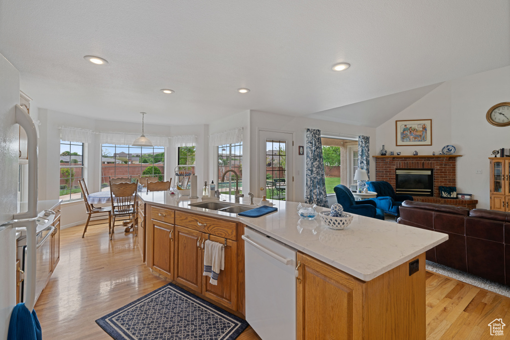 Kitchen with light wood-style flooring, a sink, plenty of natural light, white dishwasher, and a brick fireplace