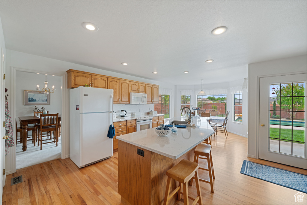 Kitchen featuring a sink, white appliances, a center island with sink, light wood-style flooring, and visible vents
