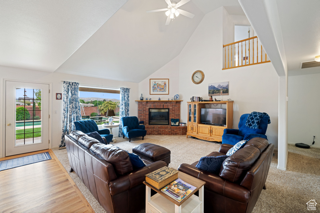 Living area featuring light wood finished floors, visible vents, a brick fireplace, high vaulted ceiling, and ceiling fan