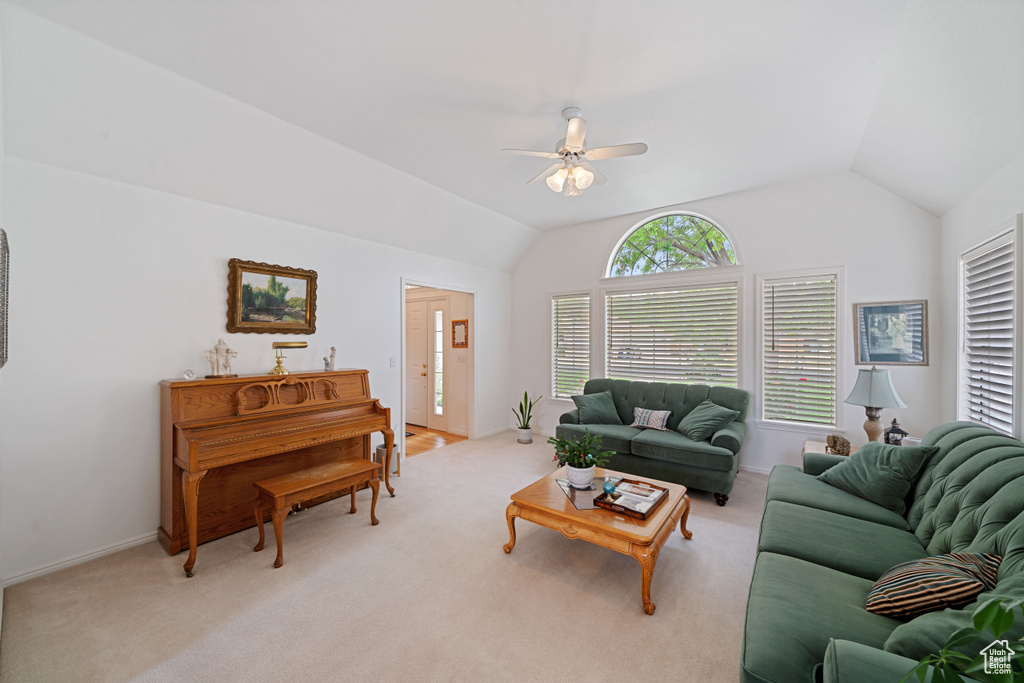 Living area featuring baseboards, vaulted ceiling, a ceiling fan, and light carpet