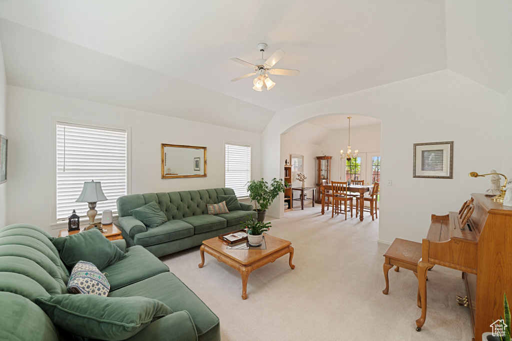 Living area with lofted ceiling, arched walkways, light colored carpet, and ceiling fan with notable chandelier