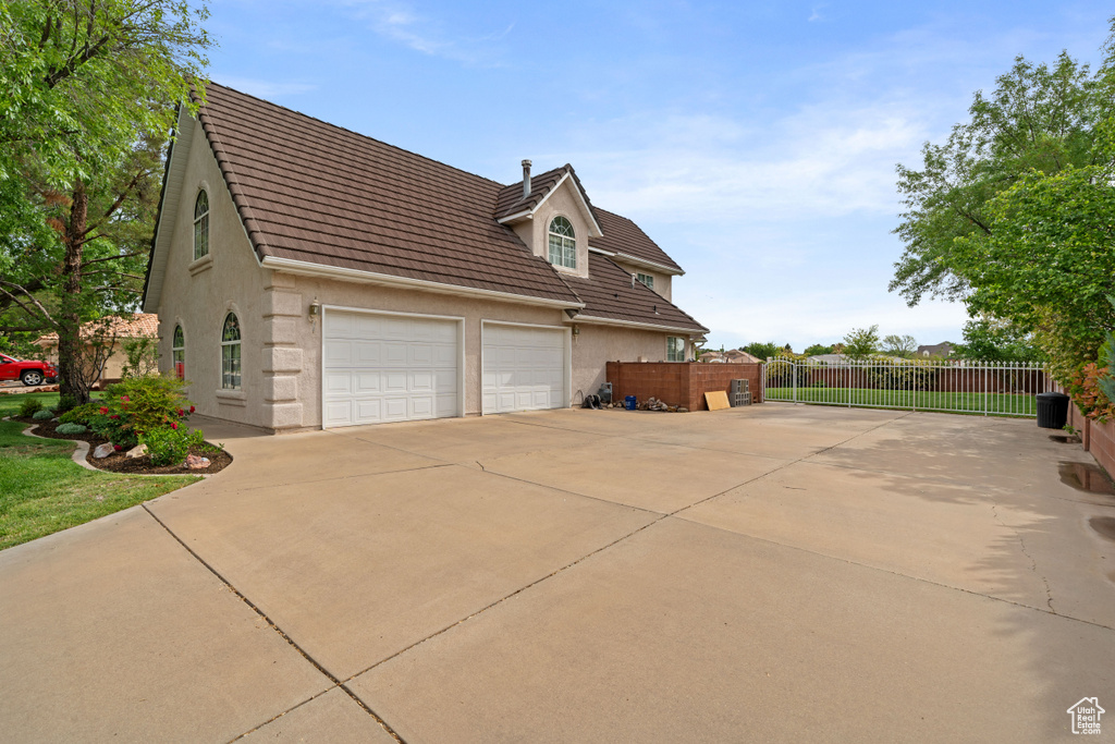 View of home's exterior featuring driveway, a tiled roof, stucco siding, and fence
