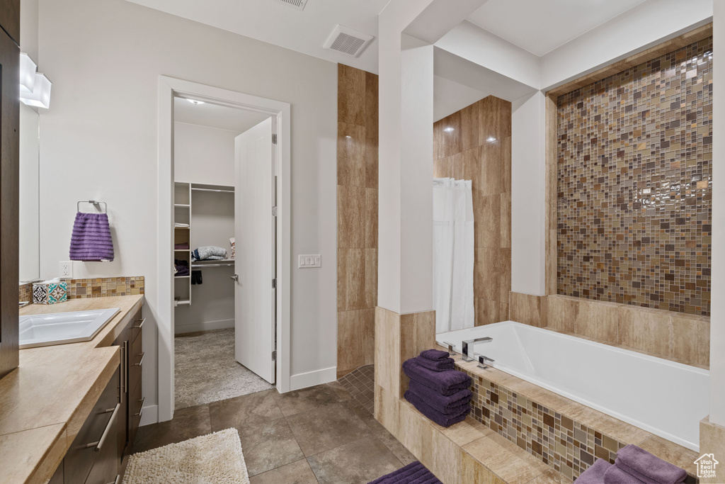 Bathroom featuring a tile shower, visible vents, vanity, a walk in closet, and tiled bath