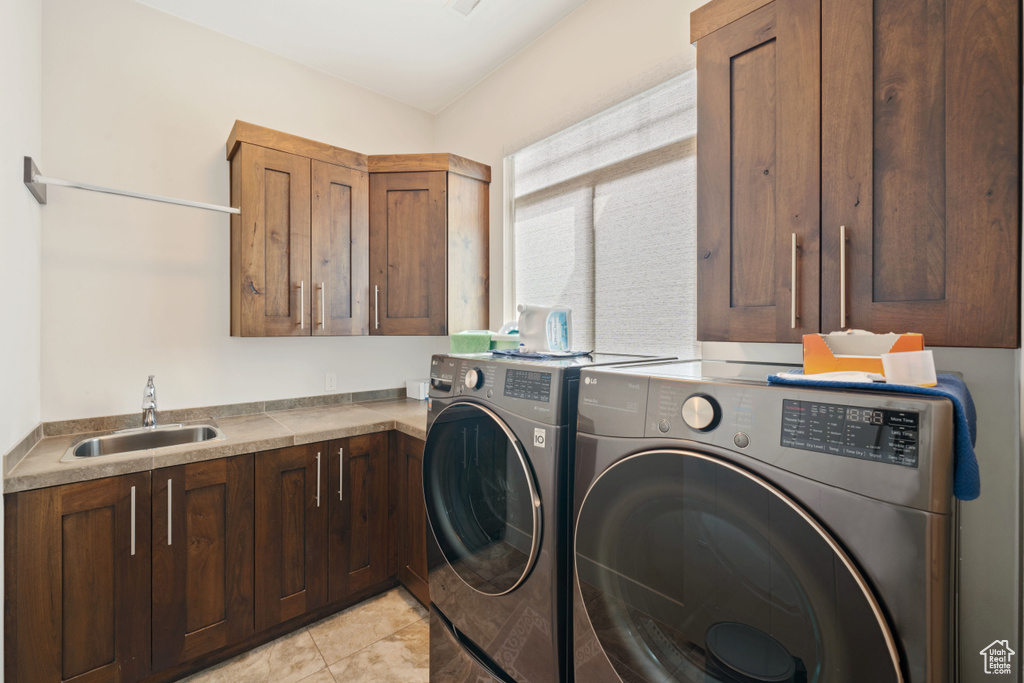 Laundry area featuring washing machine and dryer, light tile patterned flooring, a sink, and cabinet space