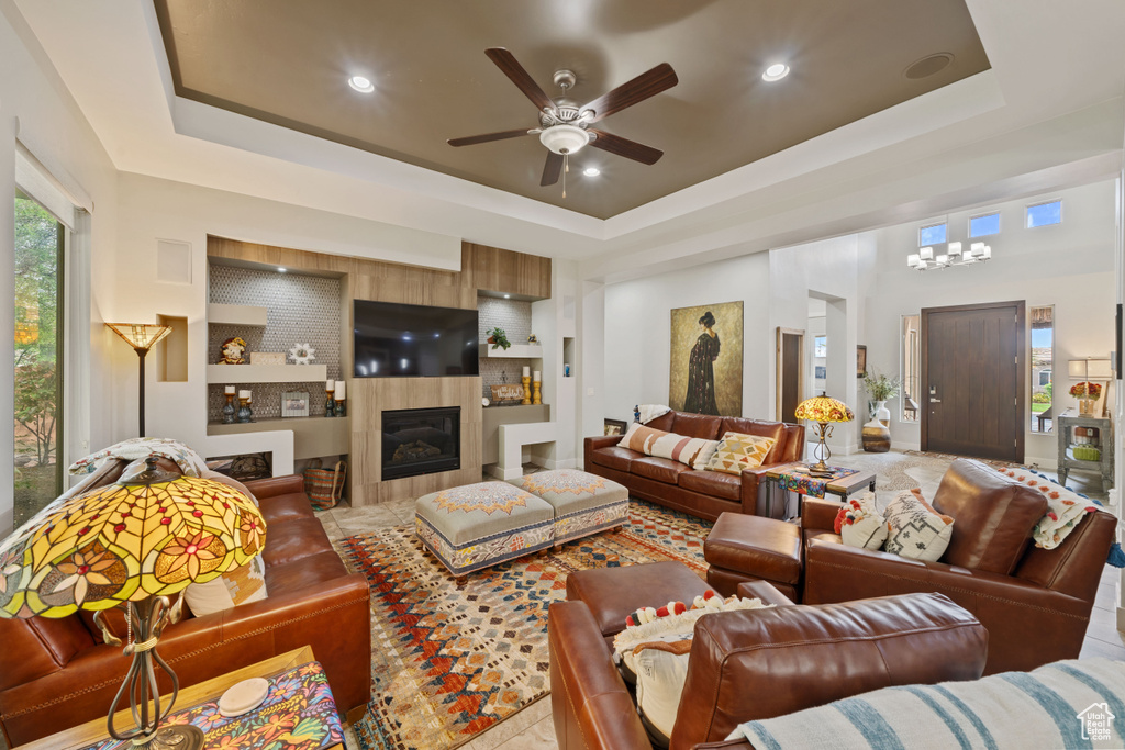 Living area featuring ceiling fan with notable chandelier, built in shelves, a tray ceiling, a tiled fireplace, and recessed lighting