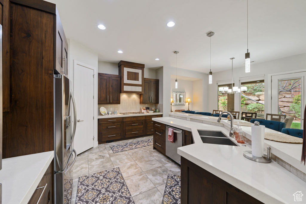 Kitchen featuring stainless steel appliances, a sink, dark brown cabinetry, decorative backsplash, and light countertops
